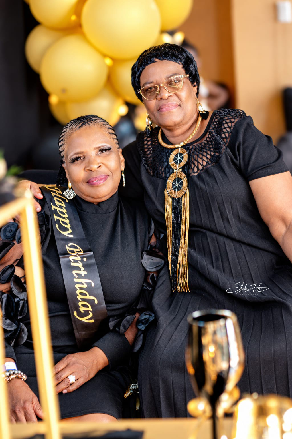 Two women celebrating beside gold birthday balloons