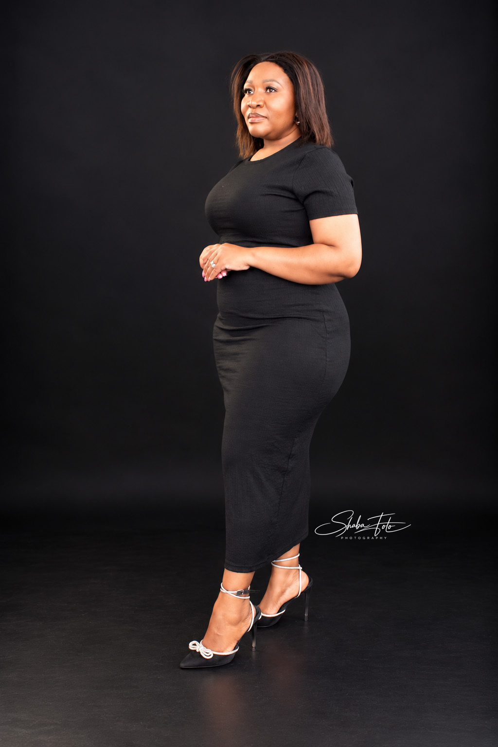Woman standing in a black dress against a dark studio backdrop